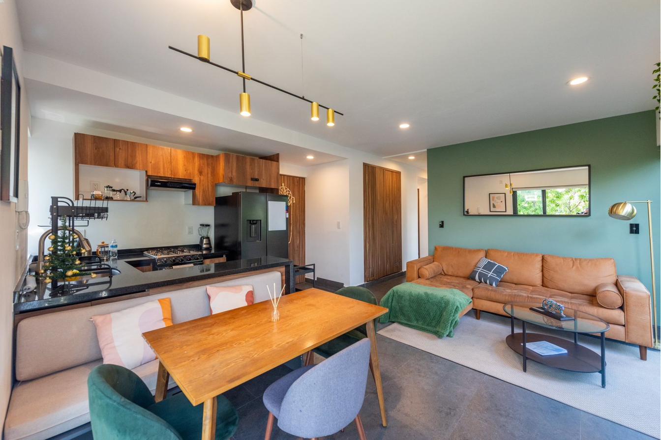 Open island kitchen flowing into dining and sala-comedor, with leather sofa and green accent wall