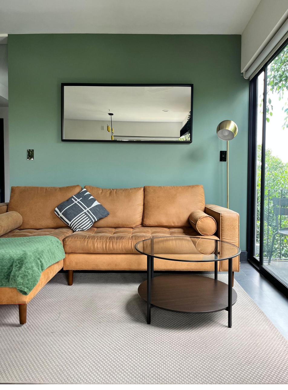 Living detail — tan leather sofa against green accent wall, brass floor lamp, ficus canopy outside