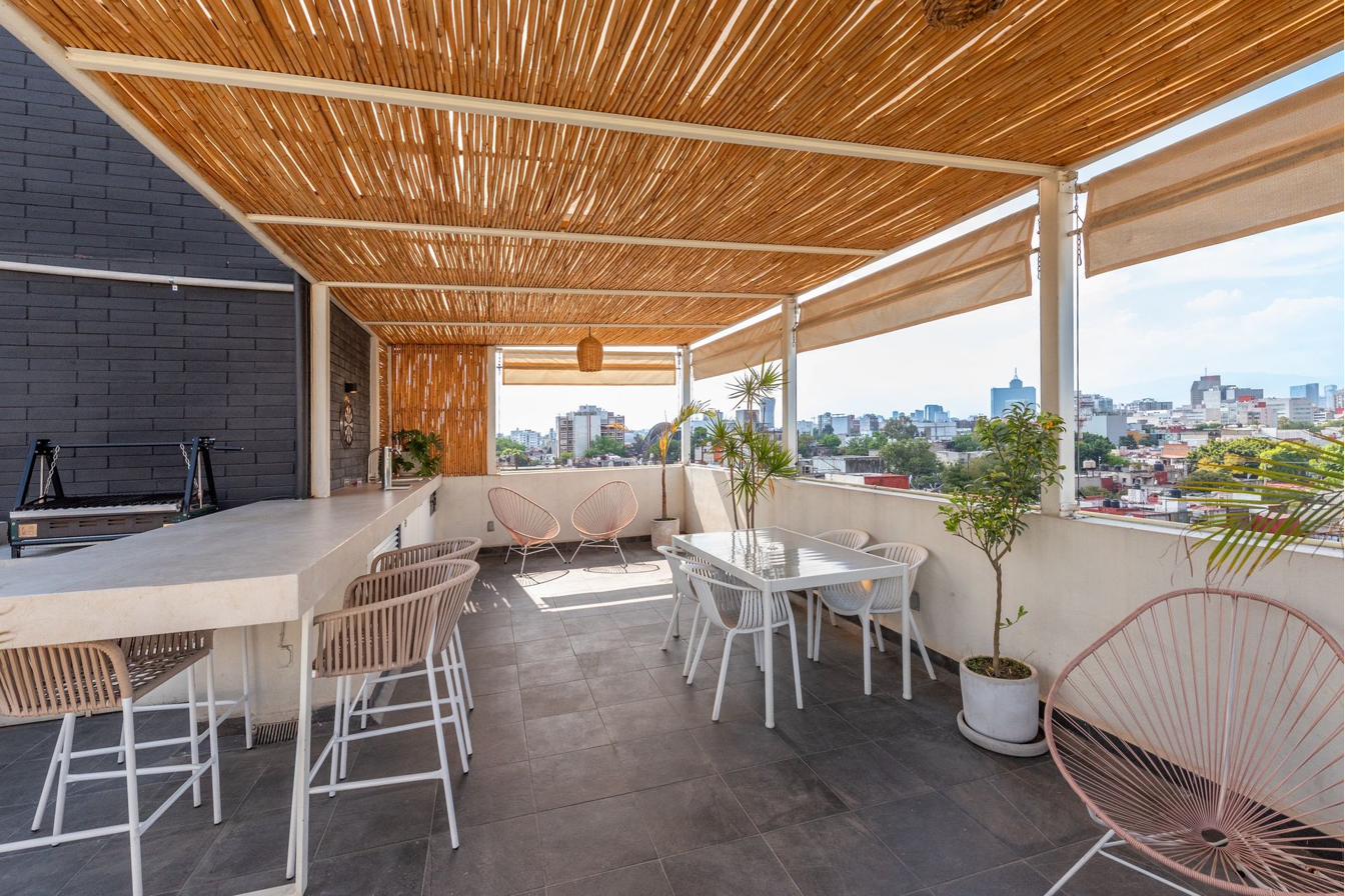 Private rooftop in daytime — pergola, concrete bar with barrel-to-tap draft beer, dartboard, dining table and skyline view